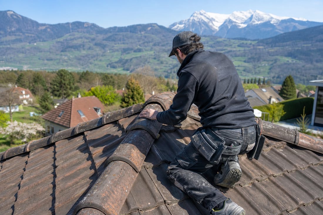 Beispiel: Dachdecker prüft seitlich kniend den Firstziegel bei einer Unterhaltskontrolle