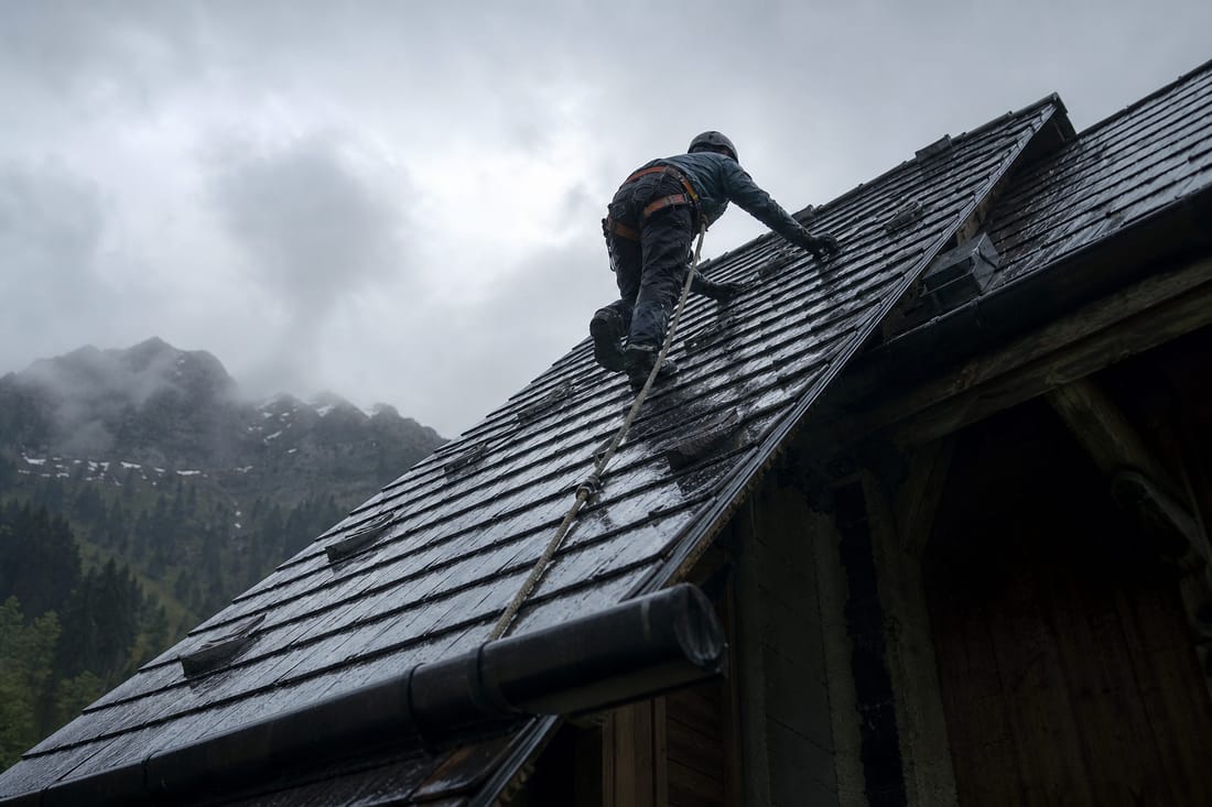 Beispiel: Dachdecker mit Sicherungsleine sichert bei Regen ein beschädigtes Dach